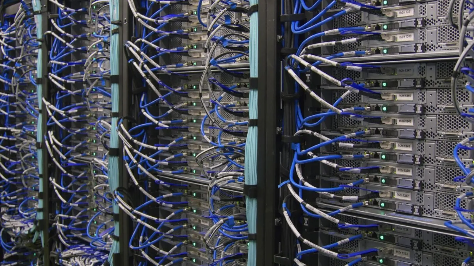Racks of servers packed with dense blue network cabling, green status lights showing along each unit.