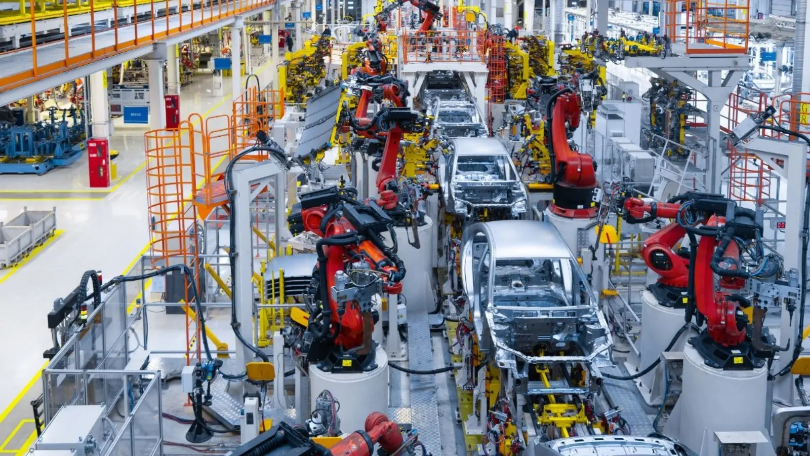 A line of part-built car bodies receding down an assembly line under overhead lighting.