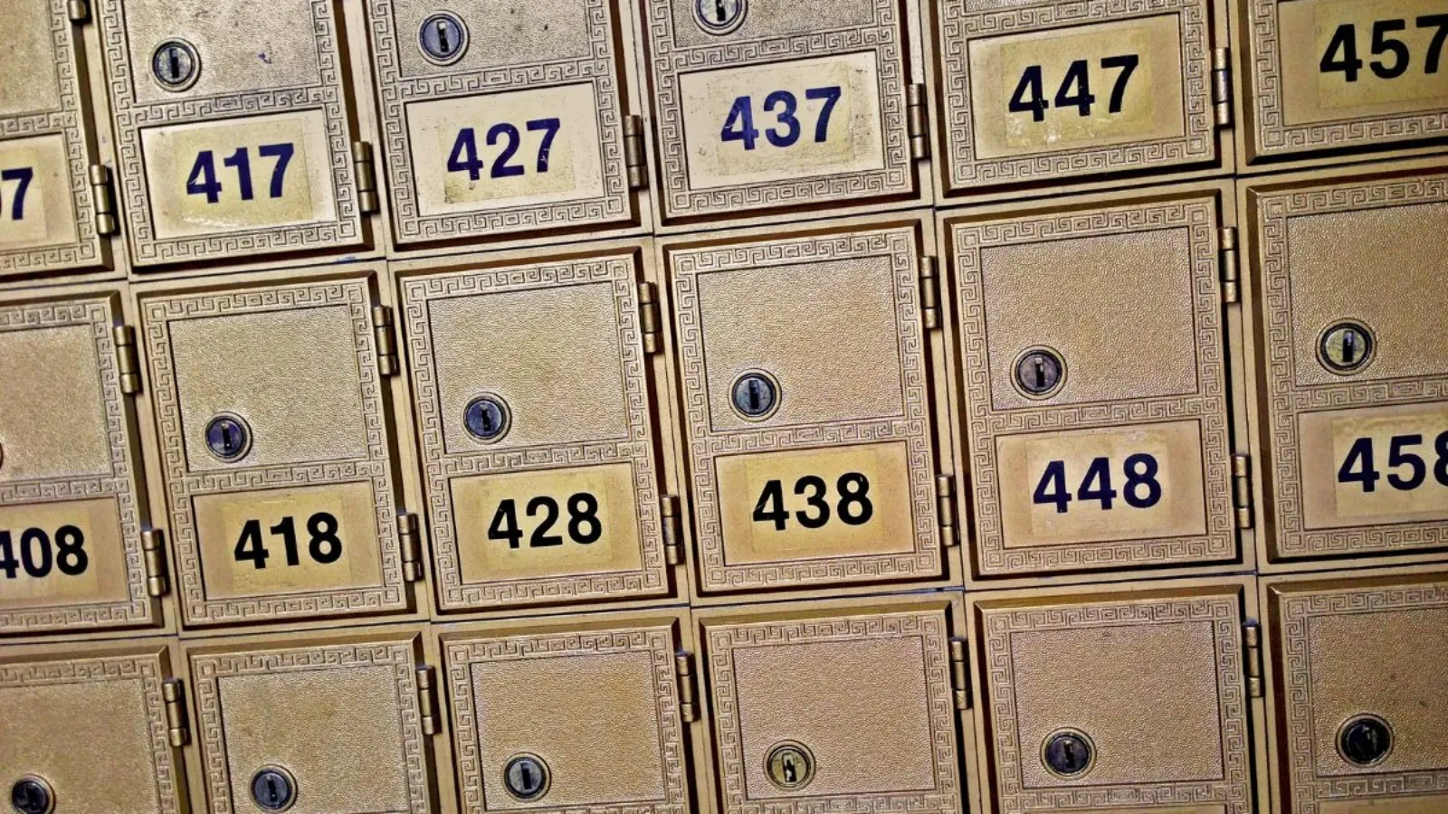 A grid of small brass mailbox doors set into a lobby wall, all closed, evenly lit.