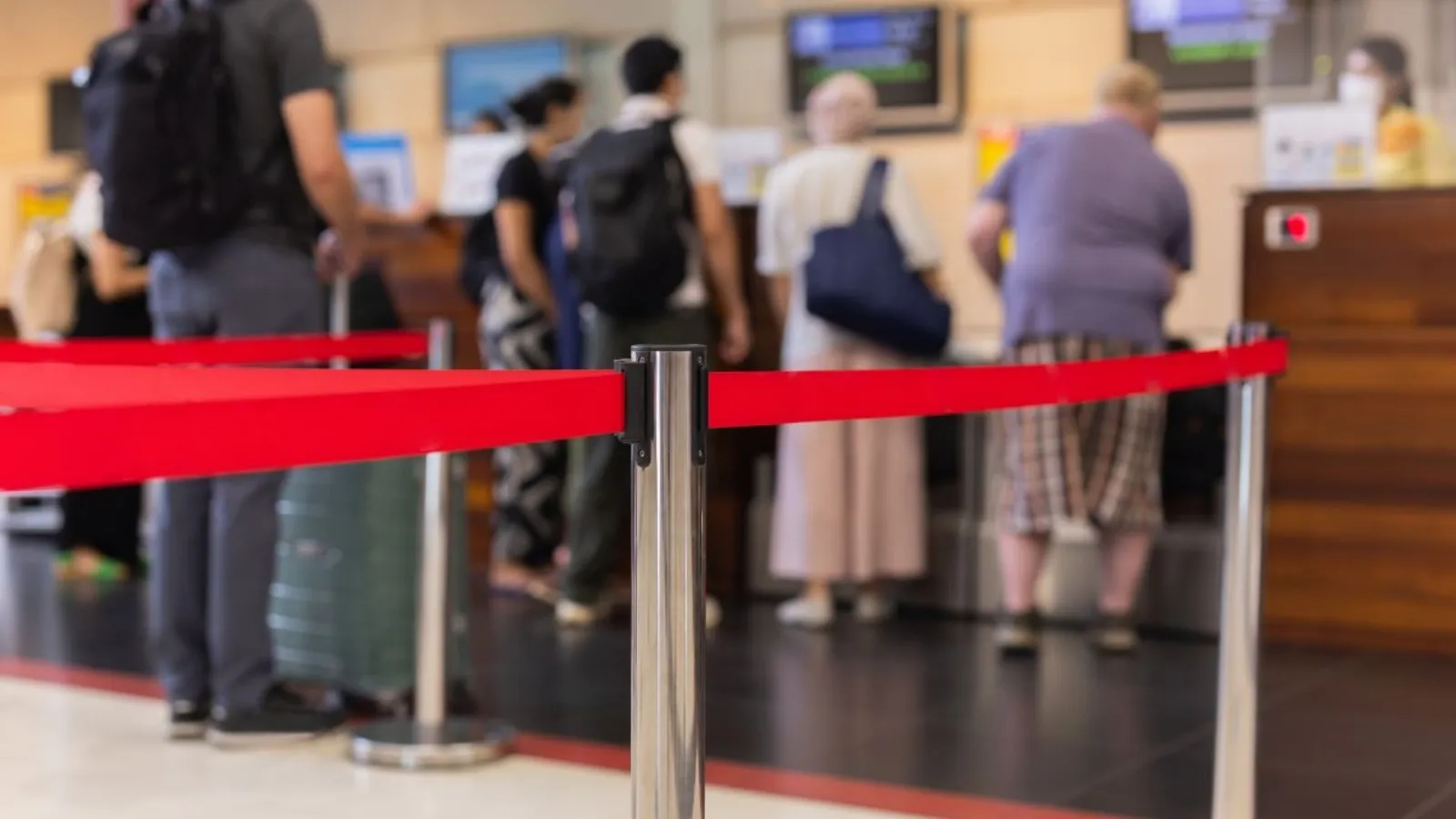 A queue of people waiting behind a red retractable barrier at a service counter.
