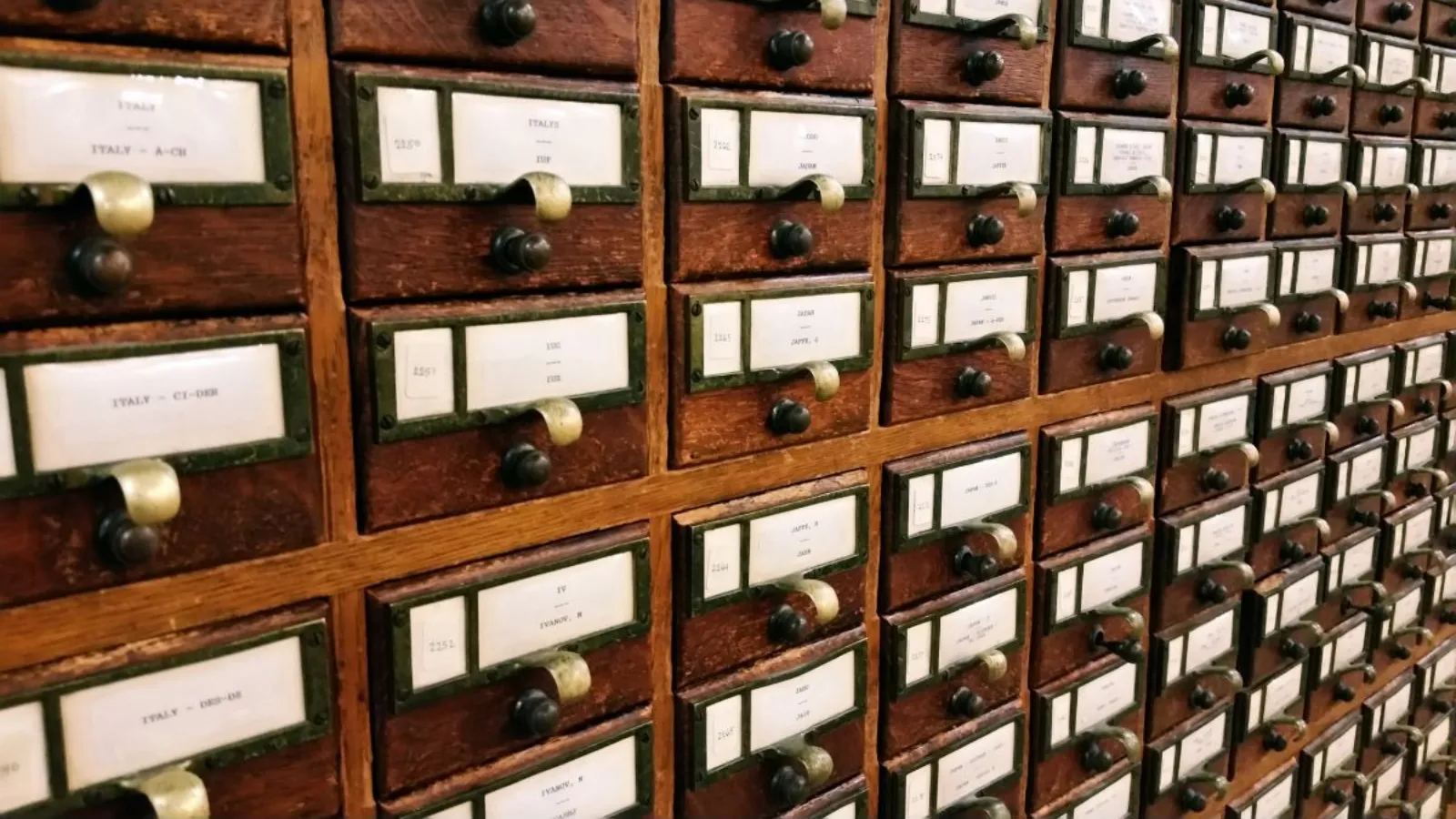 A wall of antique wooden card catalogue drawers, each with a handwritten index label.